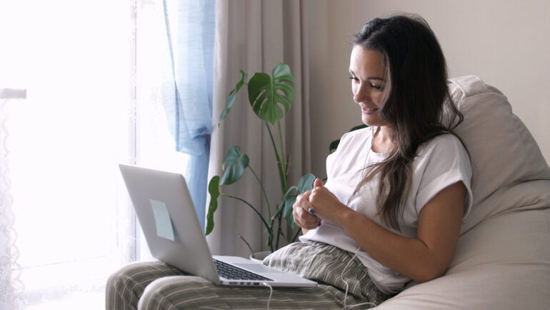 Young woman wears headset conference calling on laptop talks with online teacher studying, working from home. Lady student e learning using computer webcam chat makes notes. Distance education concept